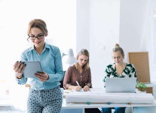 Bezpłatne zdjęcie uśmiechnięty bizneswoman patrzeje cyfrową pastylkę z jej kolegą pracuje przy tłem