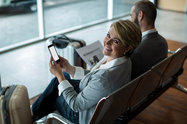 Uśmiechnięty bizneswoman z telefonu komórkowego siedzi w poczekalni