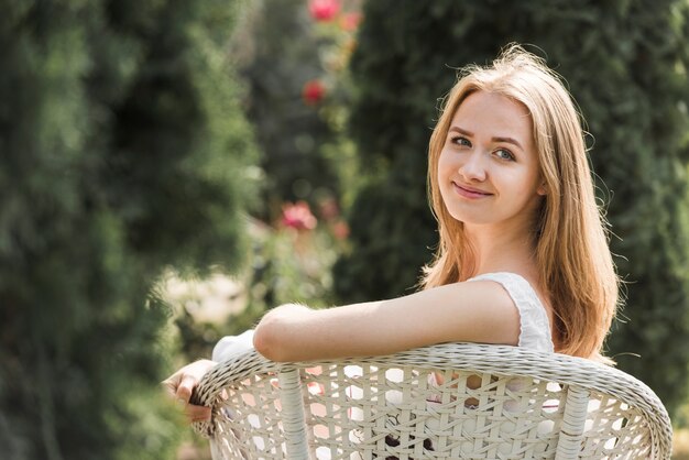 Uśmiechnięty blondynki młodej kobiety obsiadanie na ogrodowym krześle patrzeje nad ramieniem