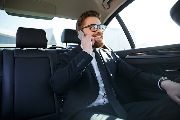 Bezpłatne zdjęcie uśmiechnięty brodaty biznesowy mężczyzna opowiada na telefonie komórkowym w eyeglasses