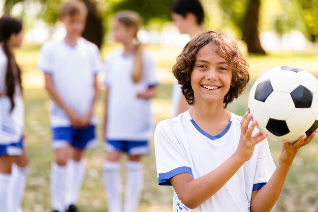 Uśmiechnięty chłopiec trzyma piłkę nożną na zewnątrz