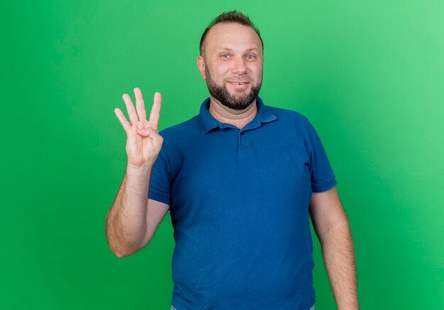 Uśmiechnięty dorosły mężczyzna słowiański pokazano cztery z ręką na białym tle na zielonej ścianie z miejsca na kopię