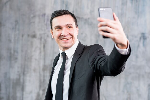 Uśmiechnięty elegancki biznesmen bierze selfie z smartphone