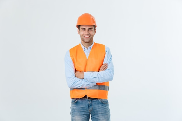 Bezpłatne zdjęcie uśmiechnięty inżynier budowlany pozowanie z rękami skrzyżowanymi. na białym tle nad szarym tłem.