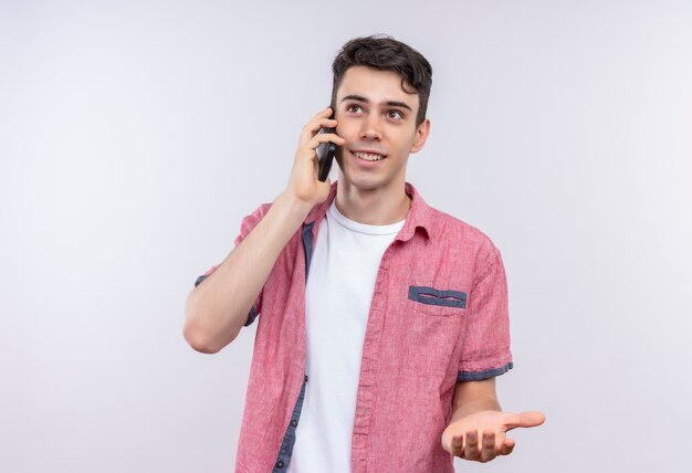 Uśmiechnięty kaukaski młody facet ubrany w różową koszulę mówi przez telefon na na białym tle