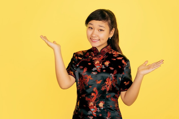 Uśmiechnięty ładny, zachęcający. Szczęśliwego chińskiego nowego roku 2020. Portret azjatyckiej młodej dziewczyny na żółtym tle. Modelka w tradycyjne stroje wygląda na szczęśliwą. Świętowanie, ludzkie emocje. Copyspace.