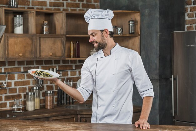 Uśmiechnięty męski szef kuchni trzyma wyśmienicie spaghetti naczynie