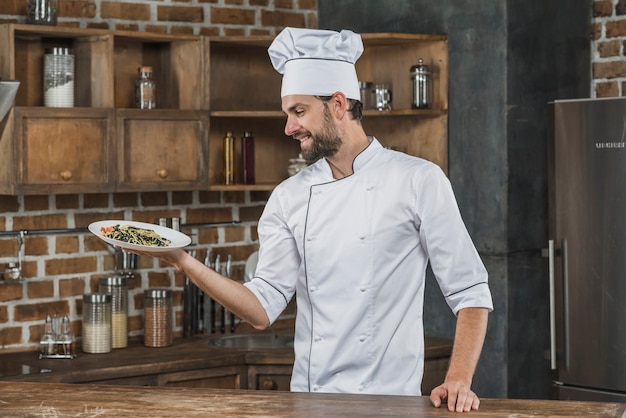 Uśmiechnięty męski szef kuchni trzyma wyśmienicie spaghetti naczynie