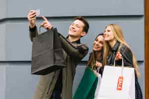 Bezpłatne zdjęcie uśmiechnięty mężczyzna bierze selfie z jego żeńskimi przyjaciela mienia torba na zakupy