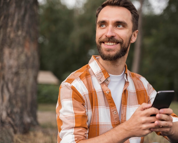 Bezpłatne zdjęcie uśmiechnięty mężczyzna na zewnątrz trzymając smartfon