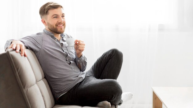 Uśmiechnięty mężczyzna pije kawę na kanapie