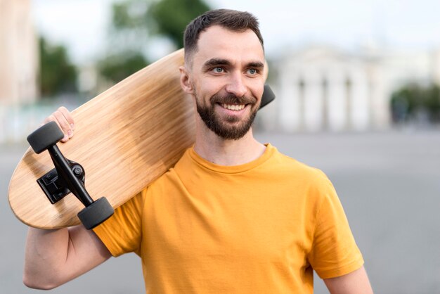 Bezpłatne zdjęcie uśmiechnięty mężczyzna trzyma deskorolkę