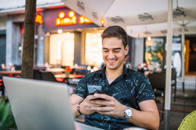 Uśmiechnięty mężczyzna używa telefon komórkowego w caf�