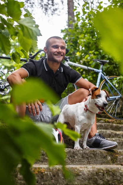 Uśmiechnięty mężczyzna z psem relaksuje się w wiosennym parku po jeździe na rowerze.