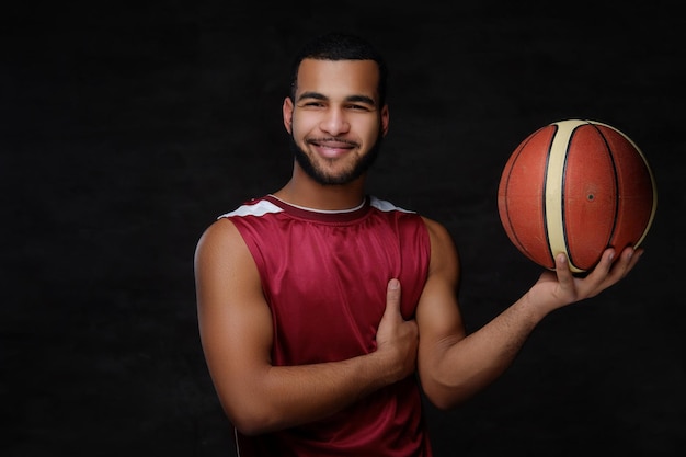 Uśmiechnięty młody afro-amerykański koszykarz w odzieży sportowej na ciemnym tle.