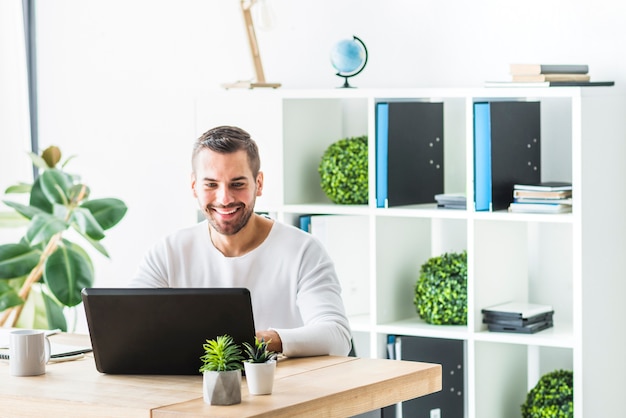 Uśmiechnięty młody biznesmen używa laptop w biurze