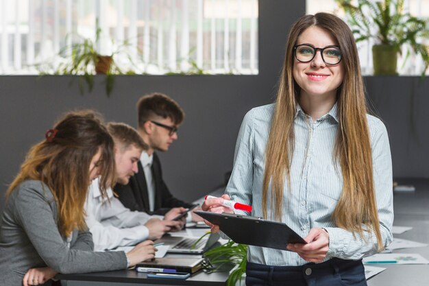 Uśmiechnięty młody bizneswoman przed kolegami pracuje w biurze