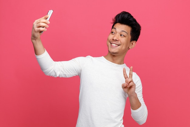 Uśmiechnięty młody człowiek robi znak pokoju przy selfie
