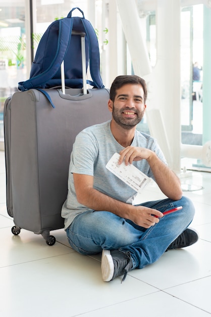 Uśmiechnięty młody człowiek siedzi blisko bagażu