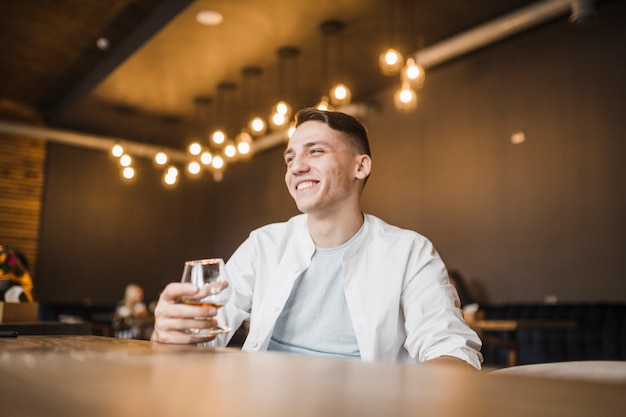 Uśmiechnięty młody człowiek trzyma szkło napój przy restauracją