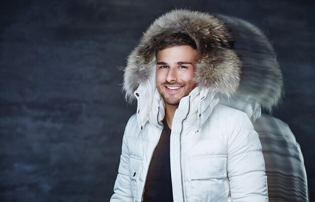Uśmiechnięty młody człowiek w zimowym ciepłym płaszczu z futrzanym kapturem.