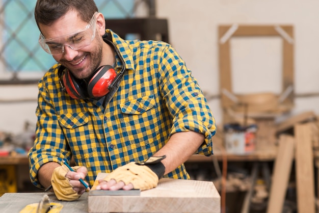 Uśmiechnięty młody męski cieśla pracuje z drewnem w jego warsztacie
