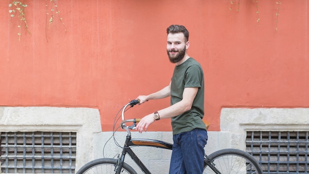 Uśmiechnięty młody męski cyklista z bicyklem przed ścianą