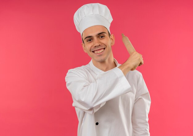 Uśmiechnięty młody mężczyzna kucharz ubrany w mundur szefa kuchni trzymając wałek do ciasta wokół ramienia z miejsca na kopię