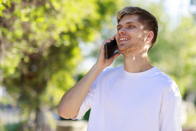 Uśmiechnięty młody mężczyzna spacerujący po parku podczas rozmowy przez telefon