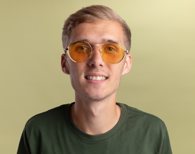 Uśmiechnięty młody przystojny facet na sobie zieloną koszulę w okularach na białym tle na oliwkowej ścianie
