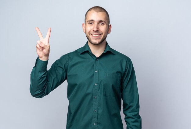Uśmiechnięty młody przystojny facet ubrany w zieloną koszulę pokazujący gest pokoju