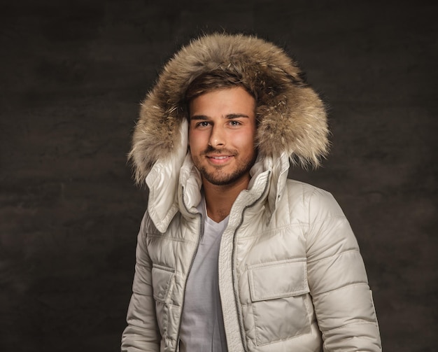 Uśmiechnięty modny mężczyzna w zimowym białym płaszczu z futrzanym kapturem.