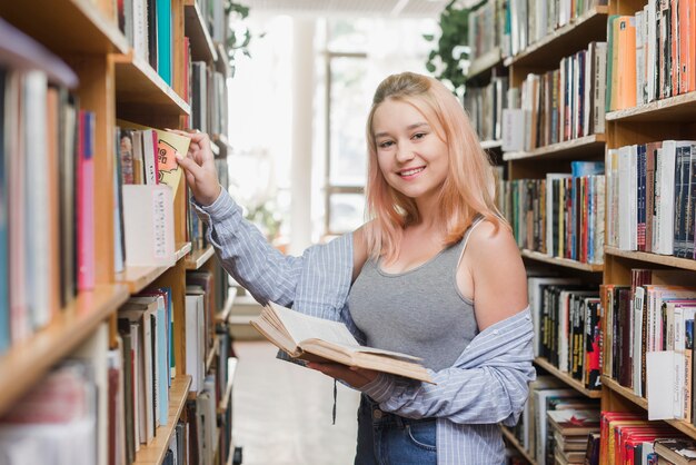 Uśmiechnięty nastolatek bierze książkę od półka na książki