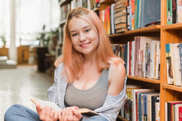 Uśmiechnięty nastolatek z książkową patrzeje kamerą