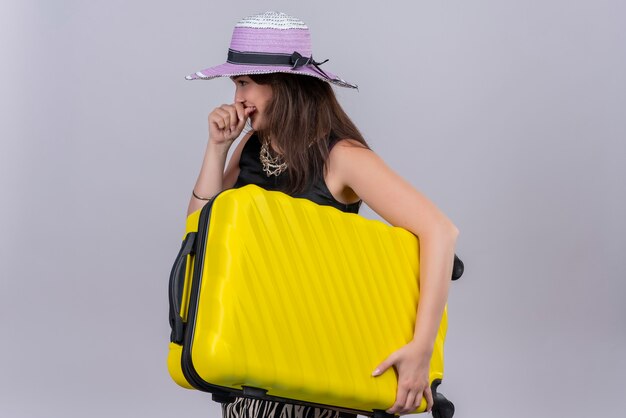 Uśmiechnięty podróżnik młoda dziewczyna ubrana w czarny podkoszulek w kapeluszu trzymając walizkę na białym tle