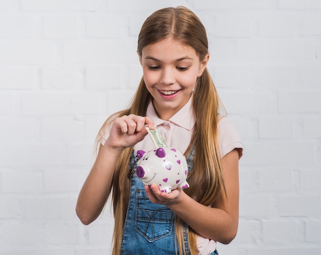 Uśmiechnięty portret dziewczyny, wstawiając banknot waluty w białym skarbonka