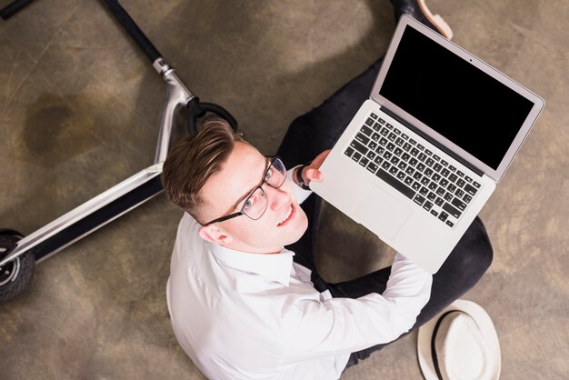 Uśmiechnięty portret młodego człowieka siedzącego na podłodze pokazano laptopa