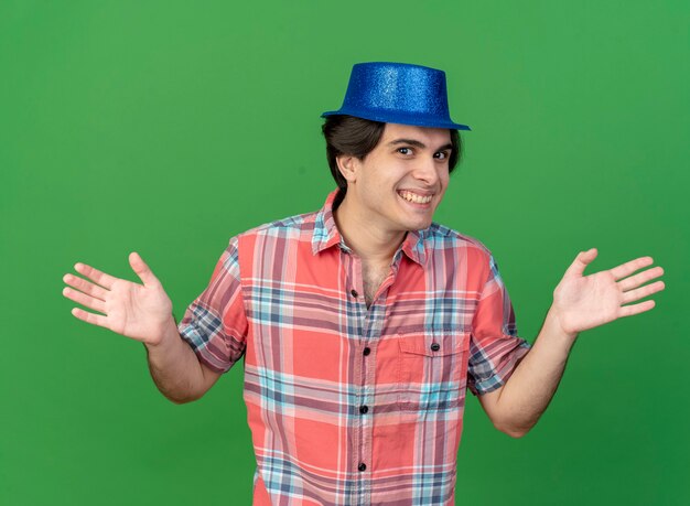 Bezpłatne zdjęcie uśmiechnięty przystojny kaukaski mężczyzna w niebieskiej imprezowej czapce trzyma otwarte ręce