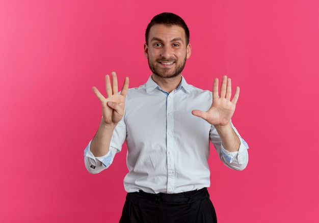 Uśmiechnięty przystojny mężczyzna gestykuluje dziewięć rękami odizolowanymi na różowej ścianie