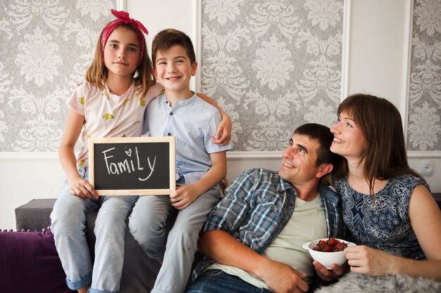 Uśmiechnięty rodzic patrzeje ich dzieci trzyma łupek z rodzinnym tekstem