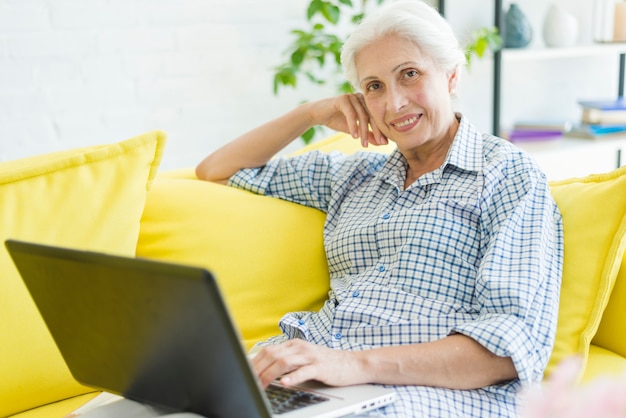 Uśmiechnięty starszy kobiety obsiadanie na kanapie z laptopem