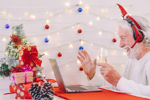Uśmiechnięty starszy mężczyzna w rozmowie wideo z laptopem świętujący boże narodzenie przy lampce wina musującego. szczęśliwego nowego roku i wesołych świąt
