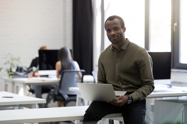 Uśmiechnięty szczęśliwy afro amerykański biznesmena obsiadanie na jego biurku