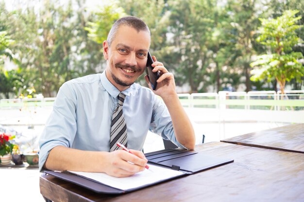 Uśmiechnięty ufny przystojny kierownik opowiada na telefonie