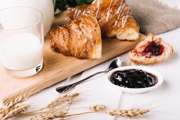 Bezpłatne zdjęcie uszy pszenicy, szklanka mleka i dżem jagody z croissant na stole