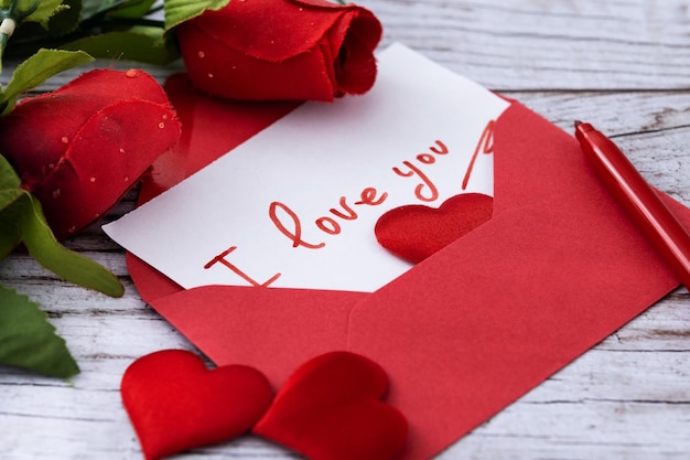 Uwaga: „Kocham cię” w kopercie z sercami i różami na drewnianym stole