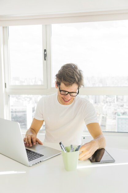 W połowie dorosły mężczyzna jest ubranym widowiska używa laptop przed szklanym okno