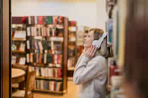 Bezpłatne zdjęcie w połowie strzału kobieta trzyma hełmofony na głowie w księgarni