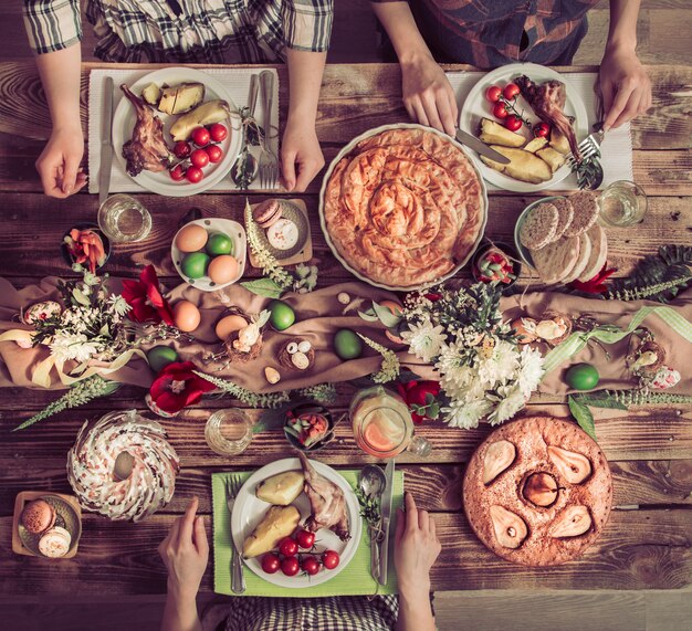 Wakacyjni przyjaciele lub rodzina przy świątecznym stole z mięsem królika, warzywami, ciastami, jajami, widokiem z góry.