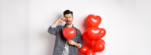 Bezpłatne zdjęcie walentynki i koncepcja miłości smutny płaczący mężczyzna trzymający balon z czerwonym sercem i biczujący łzy stojący